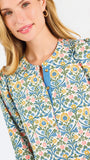 A woman modeling a three-quarter sleeve button-up blouse with a colorful floral and geometric pattern in blue, yellow, and pink, paired with blue jeans against a plain white background.