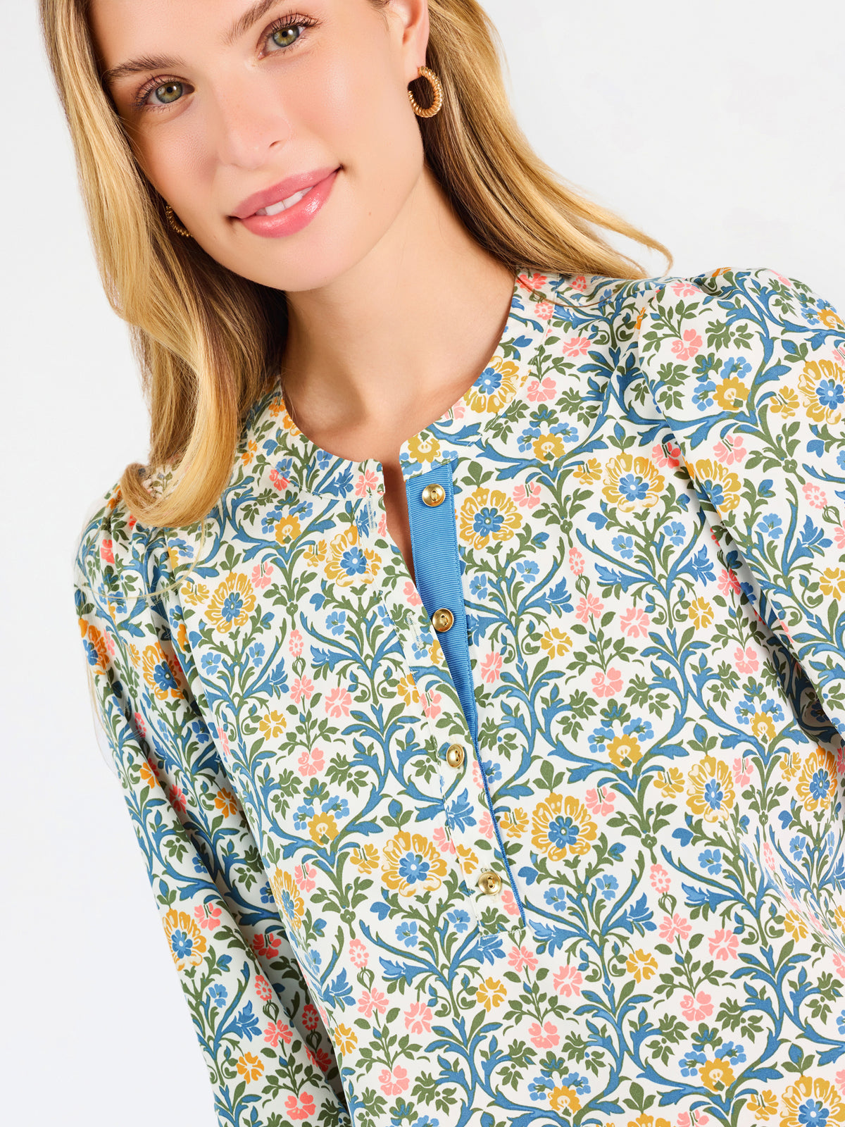 A woman modeling a three-quarter sleeve button-up blouse with a colorful floral and geometric pattern in blue, yellow, and pink, paired with blue jeans against a plain white background.