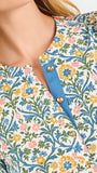 A woman modeling a three-quarter sleeve button-up blouse with a colorful floral and geometric pattern in blue, yellow, and pink, paired with blue jeans against a plain white background.