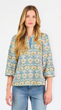 A woman modeling a three-quarter sleeve button-up blouse with a colorful floral and geometric pattern in blue, yellow, and pink, paired with blue jeans against a plain white background.