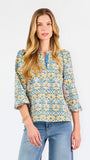  A woman modeling a three-quarter sleeve button-up blouse with a colorful floral and geometric pattern in blue, yellow, and pink, paired with blue jeans against a plain white background.
