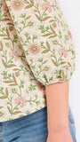 Woman wearing a tan floral blouse and jeans on a white background