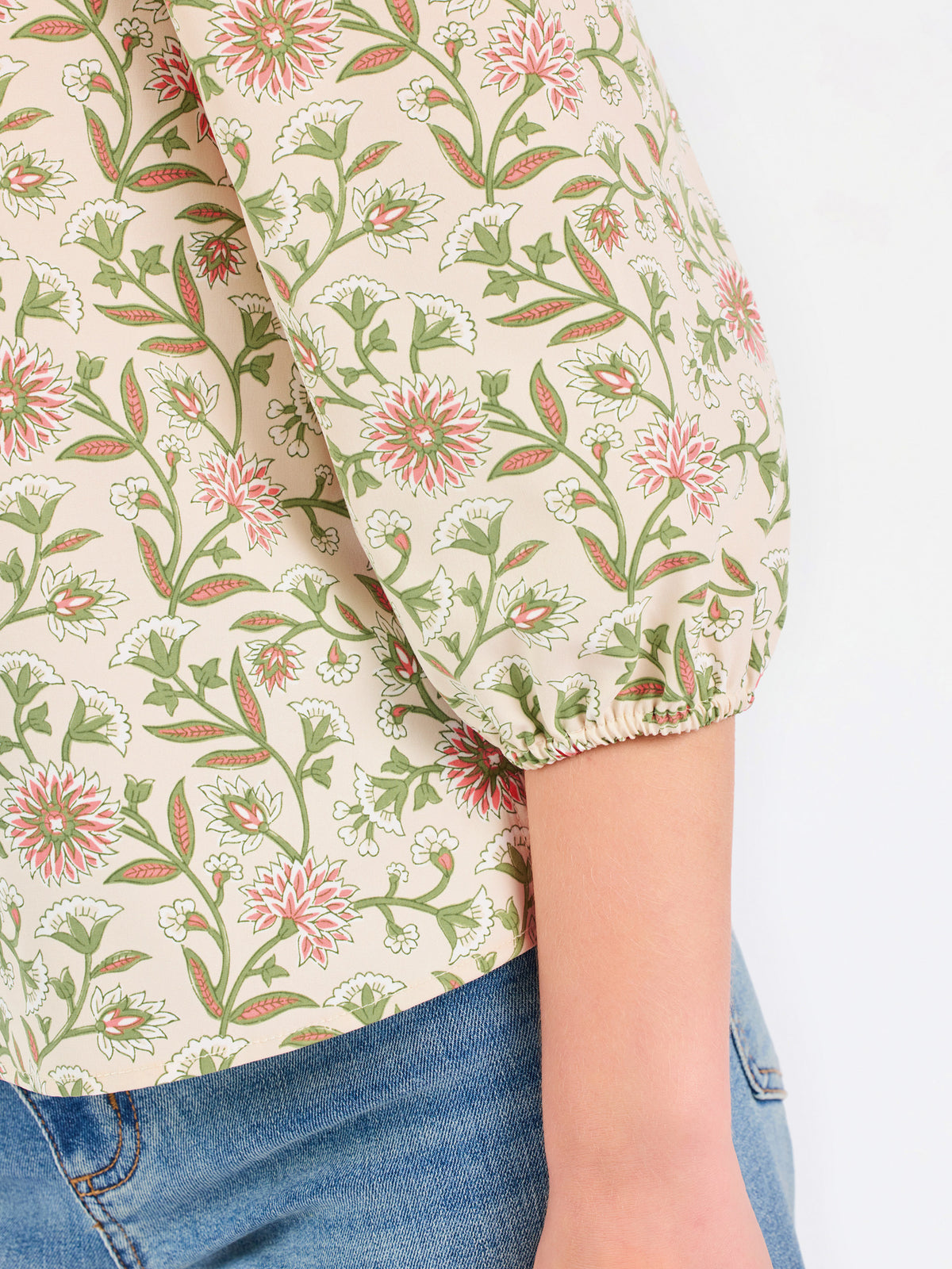 Woman wearing a tan floral blouse and jeans on a white background