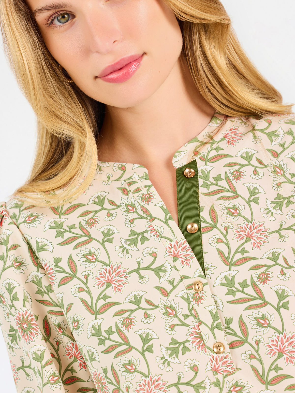 Woman wearing a tan floral blouse and jeans on a white background