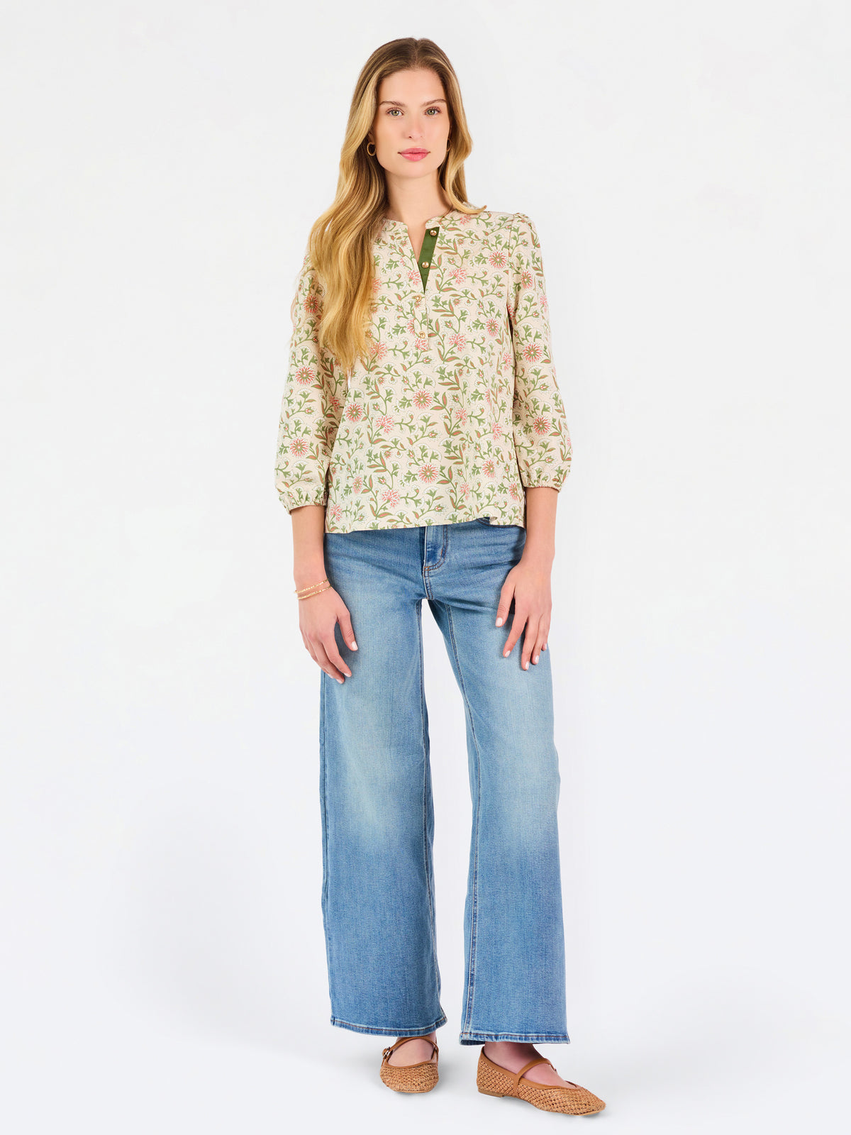 Woman wearing a tan floral blouse and jeans on a white background