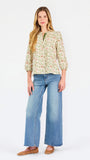 Woman wearing a tan floral blouse and jeans on a white background