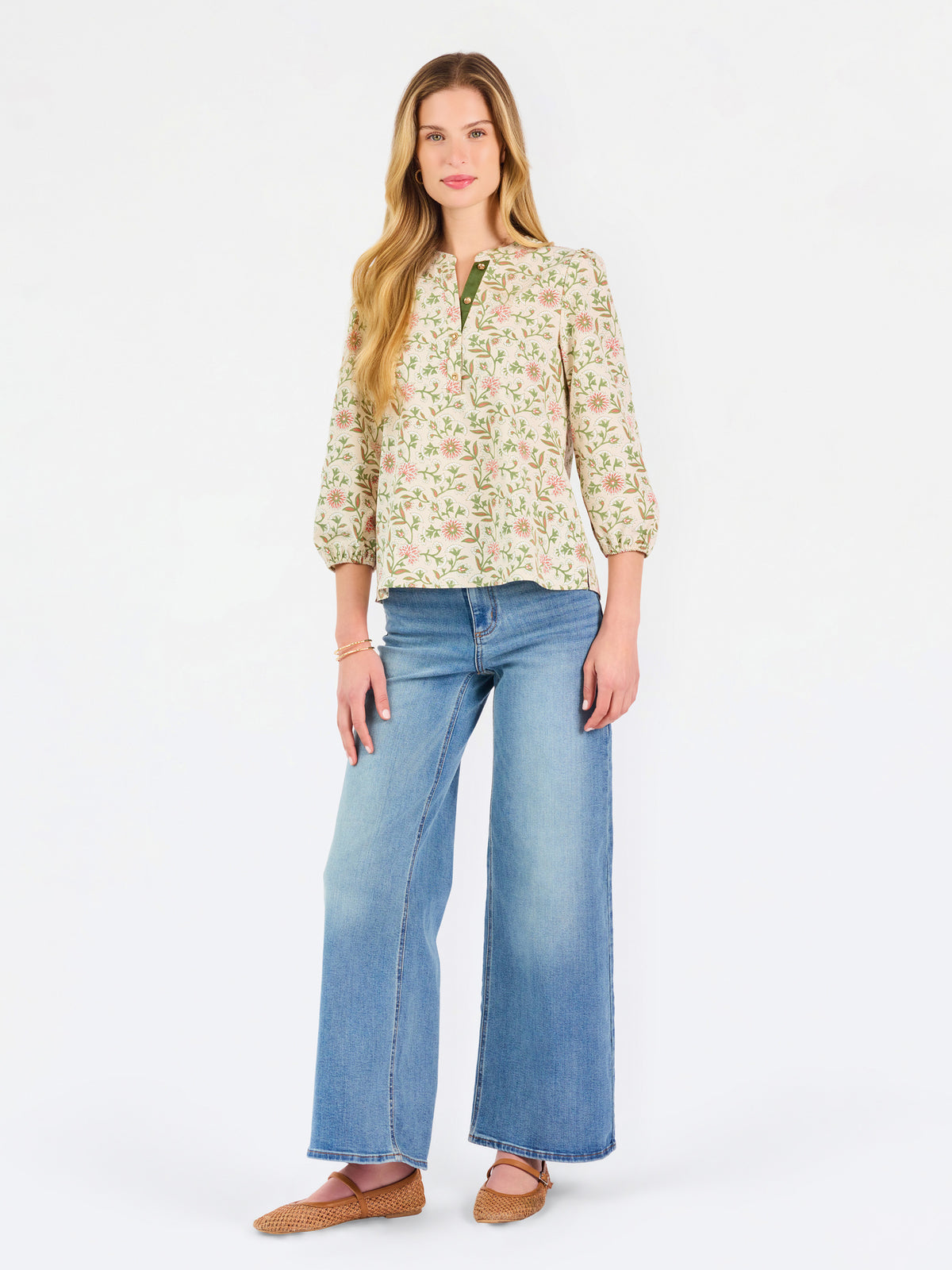 Woman wearing a tan floral blouse and jeans on a white background