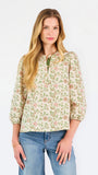 Woman wearing a tan floral blouse and jeans on a white background