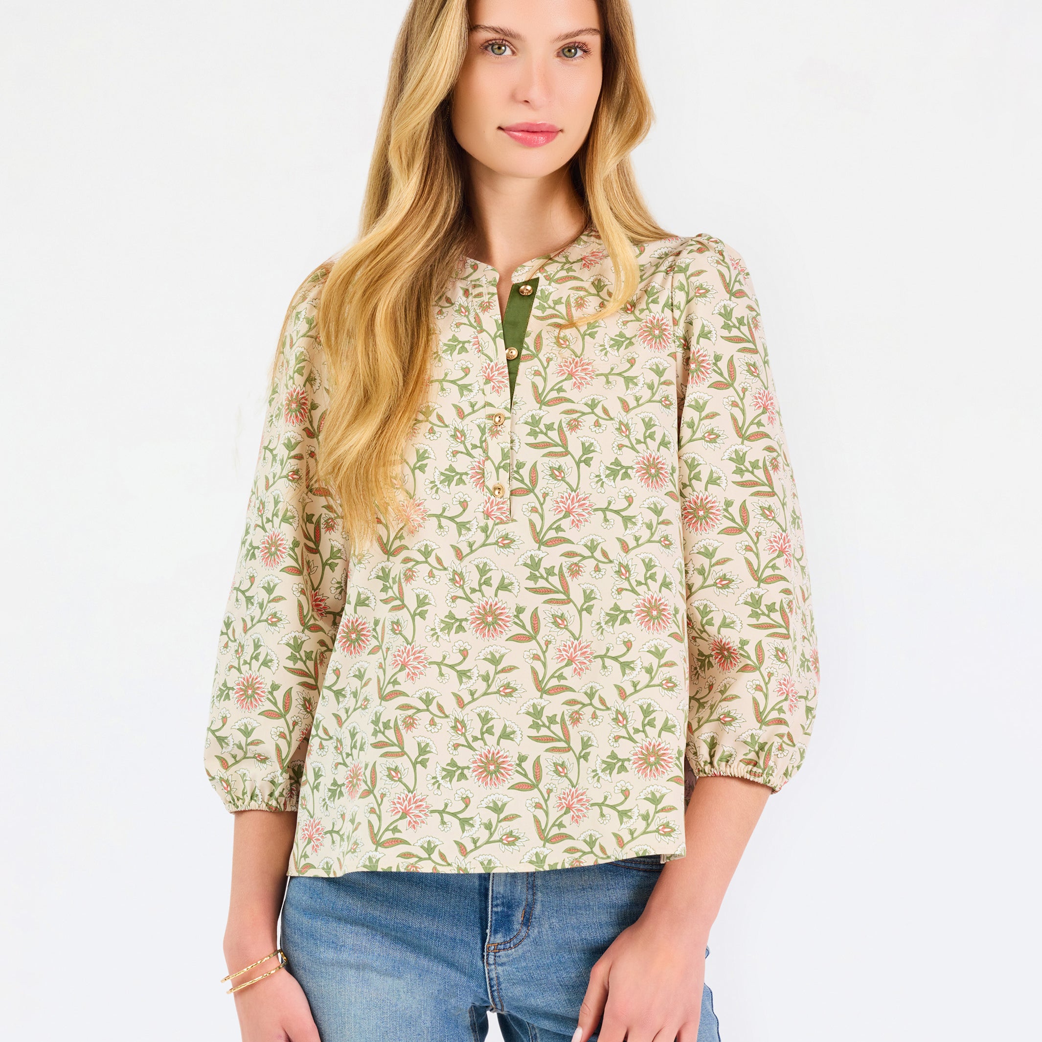Woman wearing a tan floral blouse and jeans on a white background