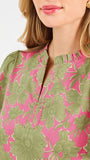 A woman modeling a short-sleeve top with a pink and olive green floral pattern, paired with blue jeans, against a plain white studio background.