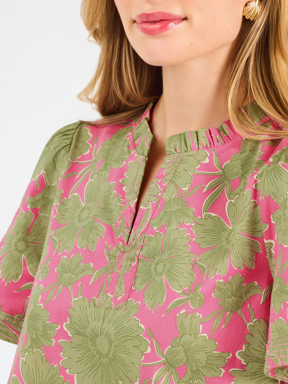 A woman modeling a short-sleeve top with a pink and olive green floral pattern, paired with blue jeans, against a plain white studio background.