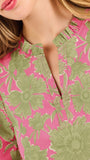 A woman modeling a short-sleeve top with a pink and olive green floral pattern, paired with blue jeans, against a plain white studio background.