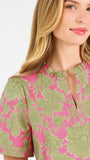A woman modeling a short-sleeve top with a pink and olive green floral pattern, paired with blue jeans, against a plain white studio background.