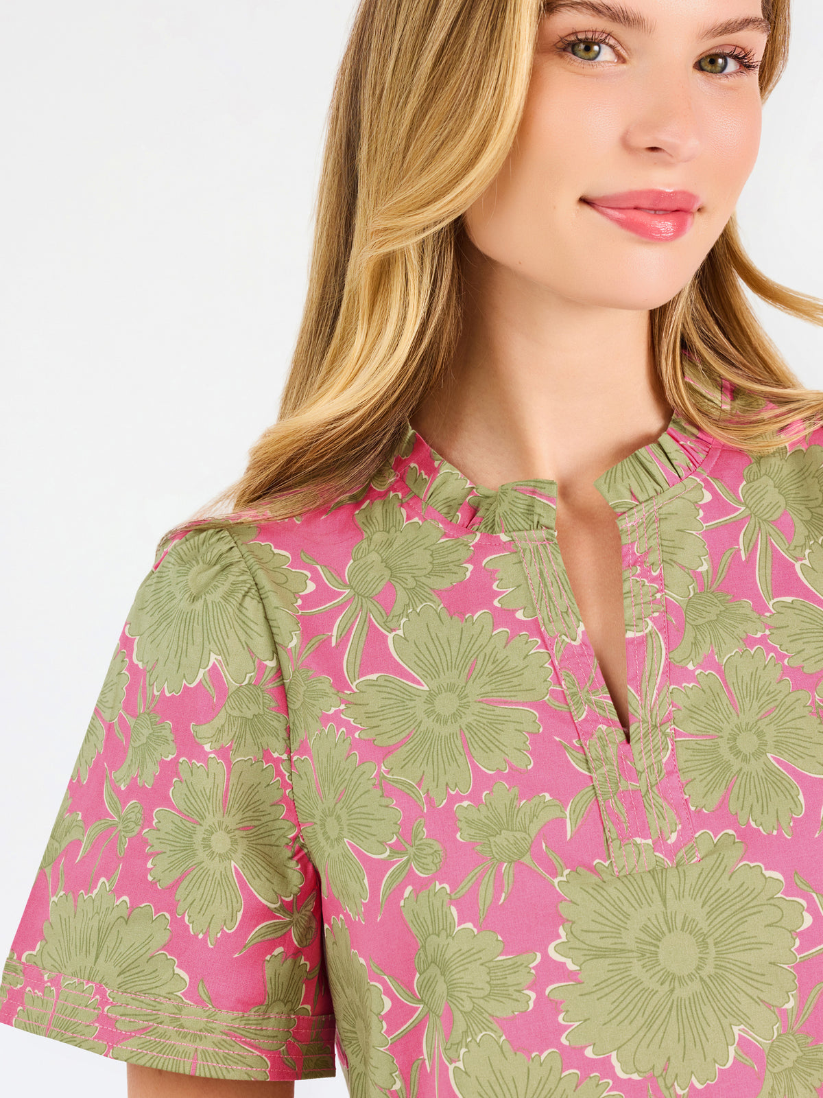 A woman modeling a short-sleeve top with a pink and olive green floral pattern, paired with blue jeans, against a plain white studio background.