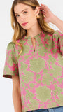 A woman modeling a short-sleeve top with a pink and olive green floral pattern, paired with blue jeans, against a plain white studio background.
