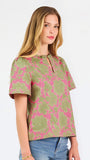 A woman modeling a short-sleeve top with a pink and olive green floral pattern, paired with blue jeans, against a plain white studio background.