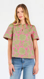 A woman modeling a short-sleeve top with a pink and olive green floral pattern, paired with blue jeans, against a plain white studio background.