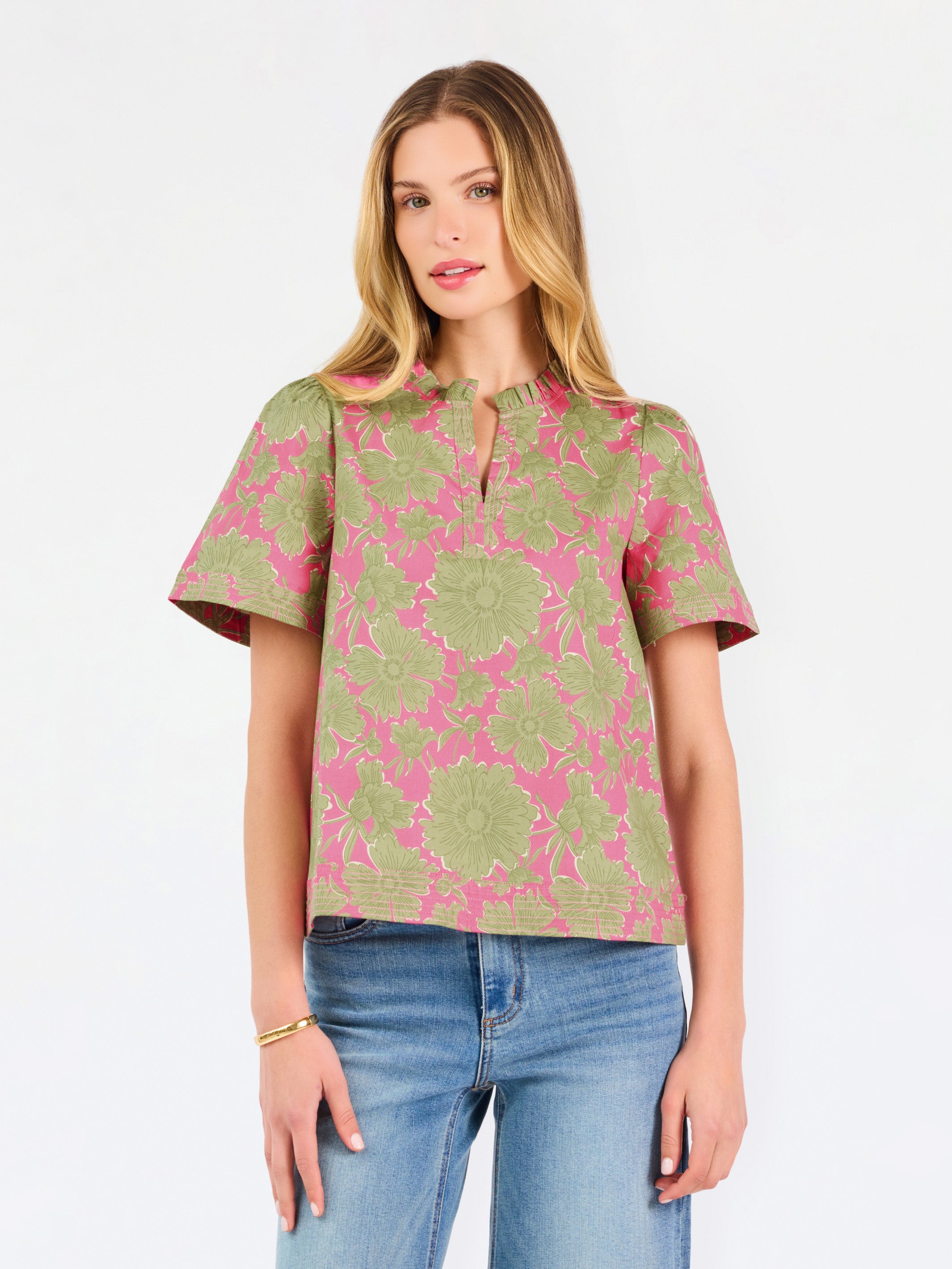 A woman modeling a short-sleeve top with a pink and olive green floral pattern, paired with blue jeans, against a plain white studio background.