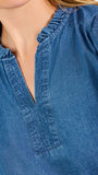 A woman modeling a blue short-sleeve puff-sleeve blouse with a split neckline, paired with cream wide-leg pants and brown flat sandals, against a plain white studio background.