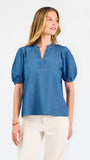 A woman modeling a blue short-sleeve puff-sleeve blouse with a split neckline, paired with cream wide-leg pants and brown flat sandals, against a plain white studio background.