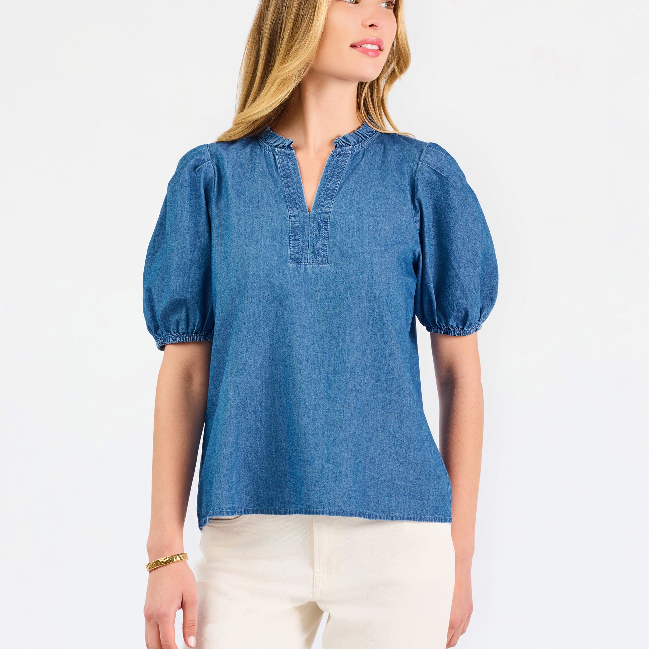 A woman modeling a blue short-sleeve puff-sleeve blouse with a split neckline, paired with cream wide-leg pants and brown flat sandals, against a plain white studio background.