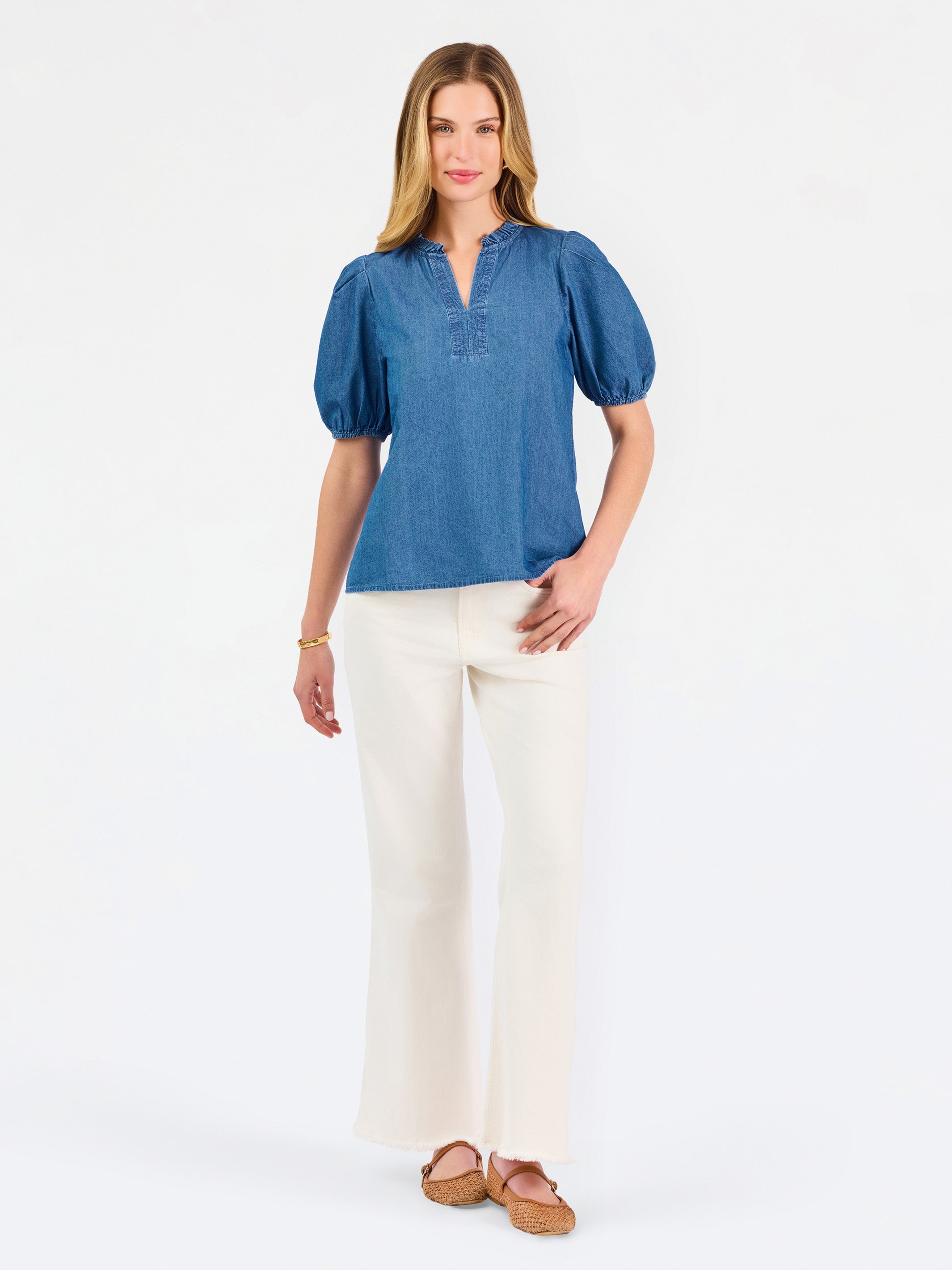 A woman modeling a blue short-sleeve puff-sleeve blouse with a split neckline, paired with cream wide-leg pants and brown flat sandals, against a plain white studio background.