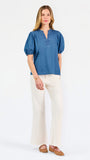 A woman modeling a blue short-sleeve puff-sleeve blouse with a split neckline, paired with cream wide-leg pants and brown flat sandals, against a plain white studio background.