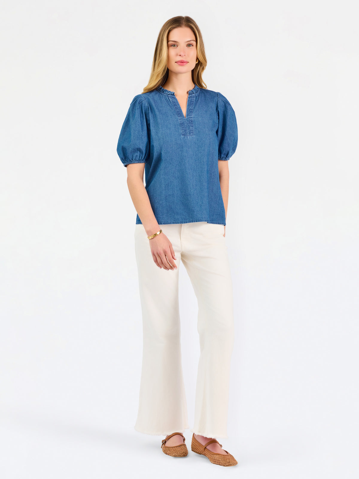 A woman modeling a blue short-sleeve puff-sleeve blouse with a split neckline, paired with cream wide-leg pants and brown flat sandals, against a plain white studio background.