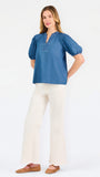 A woman modeling a blue short-sleeve puff-sleeve blouse with a split neckline, paired with cream wide-leg pants and brown flat sandals, against a plain white studio background.