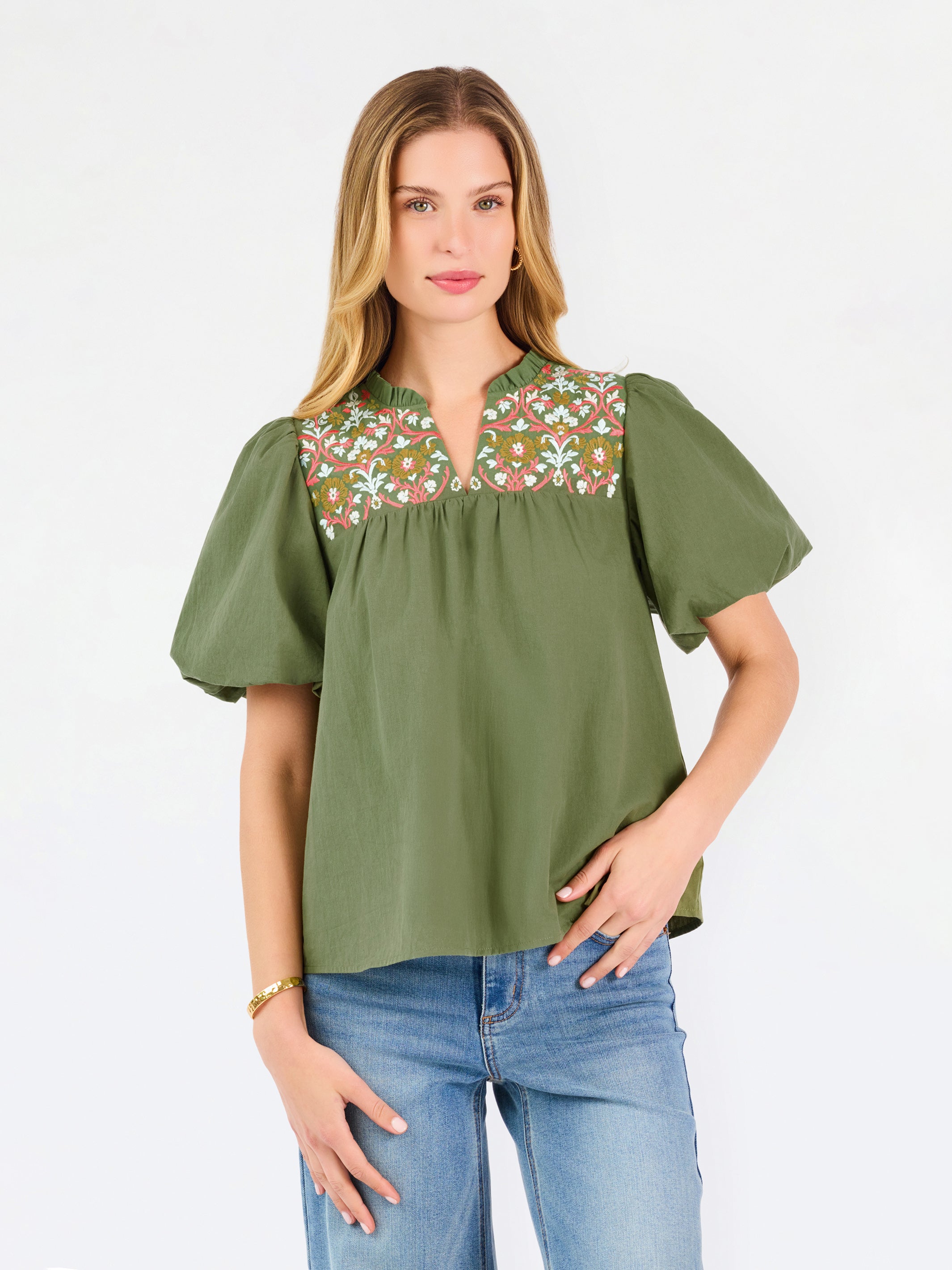 Woman wearing a green blouse with floral embroidery and blue jeans on a white background