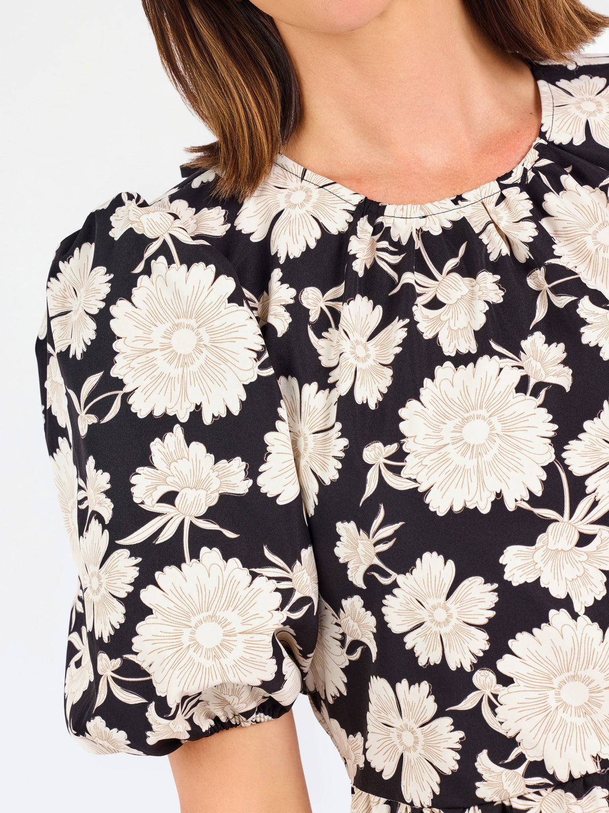 A woman modeling a black puff-sleeve blouse with a large white floral pattern, paired with blue jeans, against a plain white studio background.