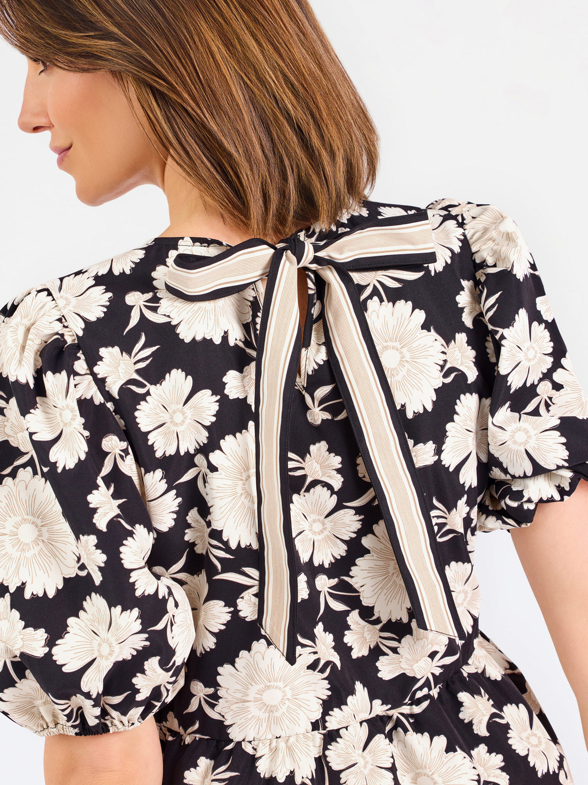 Close-up back view of a woman wearing a black top with a large cream floral print and a tied bow at the neckline.
