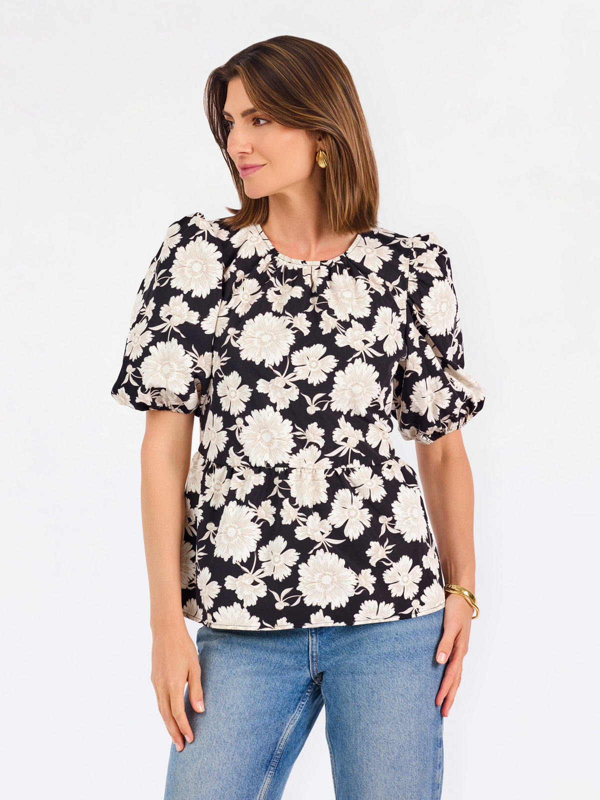 A woman modeling a black puff-sleeve blouse with a large white floral pattern, paired with blue jeans, against a plain white studio background.