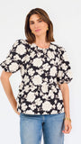 A woman modeling a black puff-sleeve blouse with a large white floral pattern, paired with blue jeans, against a plain white studio background.