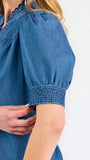 Blonde woman wearing a short sleeve denim colored top with navy scalloped trim