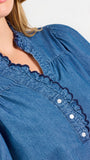 Blonde woman wearing a short sleeve denim colored top with navy scalloped trim