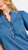 Blonde woman wearing a short sleeve denim colored top with navy scalloped trim