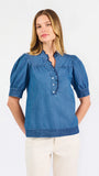 Blonde woman wearing a short sleeve denim colored top with navy scalloped trim