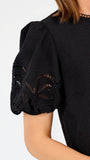 Short haired brunette woman wearing a short sleeve black colored top with cut out detail on puff sleeves