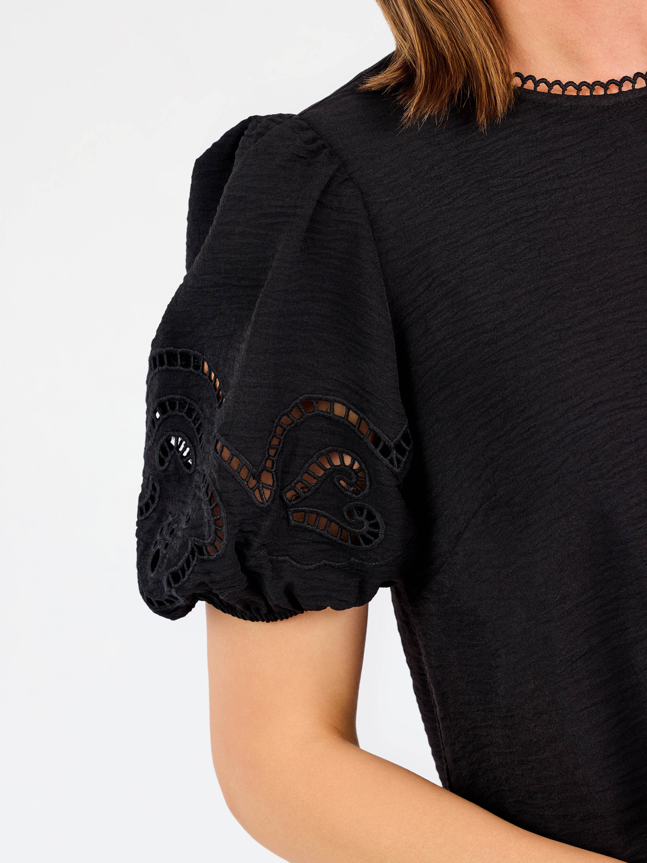 Short haired brunette woman wearing a short sleeve black colored top with cut out detail on puff sleeves
