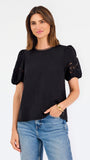 Short haired brunette woman wearing a short sleeve black colored top with cut out detail on puff sleeves