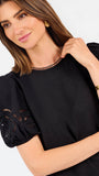 Short haired brunette woman wearing a short sleeve black colored top with cut out detail on puff sleeves