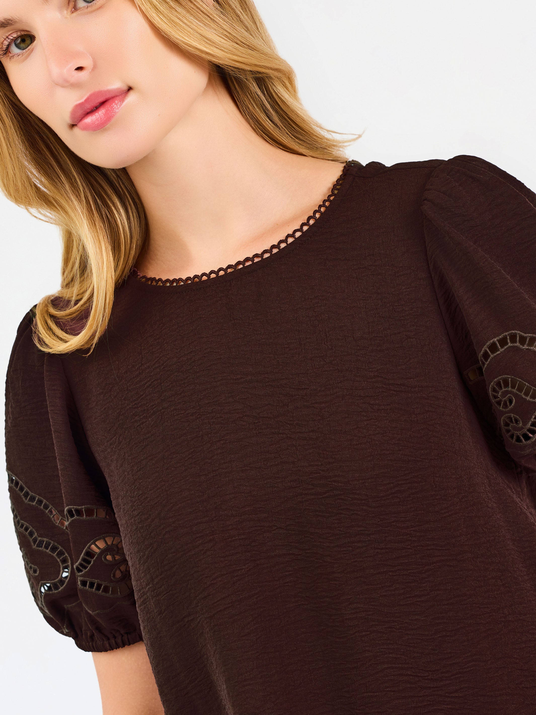 Blonde woman wearing a short sleeve brown colored top with cut out detail on puff sleeves