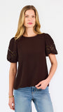 Blonde woman wearing a short sleeve brown colored top with cut out detail on puff sleeves
