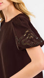 Blonde woman wearing a short sleeve brown colored top with cut out detail on puff sleeves