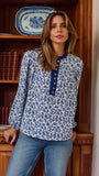 A woman wearing a blue and white floral print long-sleeve blouse with a buttoned collar, standing in front of a wooden bookshelf.