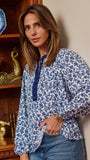 A woman wearing a blue and white floral print long-sleeve blouse with a buttoned collar, standing in front of a wooden bookshelf.