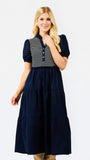 A woman modeling a navy blue tiered midi dress with a navy and white striped button-up bodice and puff sleeves, set against a plain white studio background.