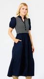 A woman modeling a navy blue midi dress with a navy and white striped bodice, short puff sleeves, and a tiered skirt, set against a plain white studio background.