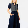 A woman modeling a navy blue midi dress with a navy and white striped bodice, short puff sleeves, and a tiered skirt, set against a plain white studio background.